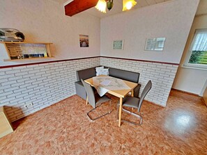 A corner room with a brick wall, a table with chairs, a bench, and a window with a view. - Groth Holiday Apartments (Heringsdorf)