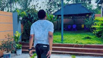 A person standing on a concrete path with grass patches, facing a basketball hoop.