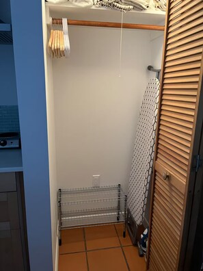 A small, enclosed space with a metal drying rack, a wooden door, and a patterned curtain. - Serenity Now Guest House (Los Angeles)
