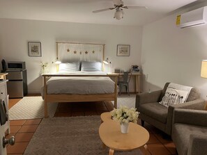 A bedroom with a bed, bedside tables, a desk, a chair, a sofa, a coffee table with flowers, a ceiling fan, and an air conditioning unit. - Serenity Now Guest House (Los Angeles)