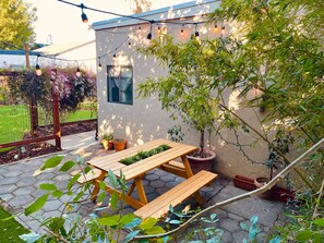 A patio area with wooden benches and a table, surrounded by potted plants and a string of lights. - Serenity Now Guest House (Los Angeles)