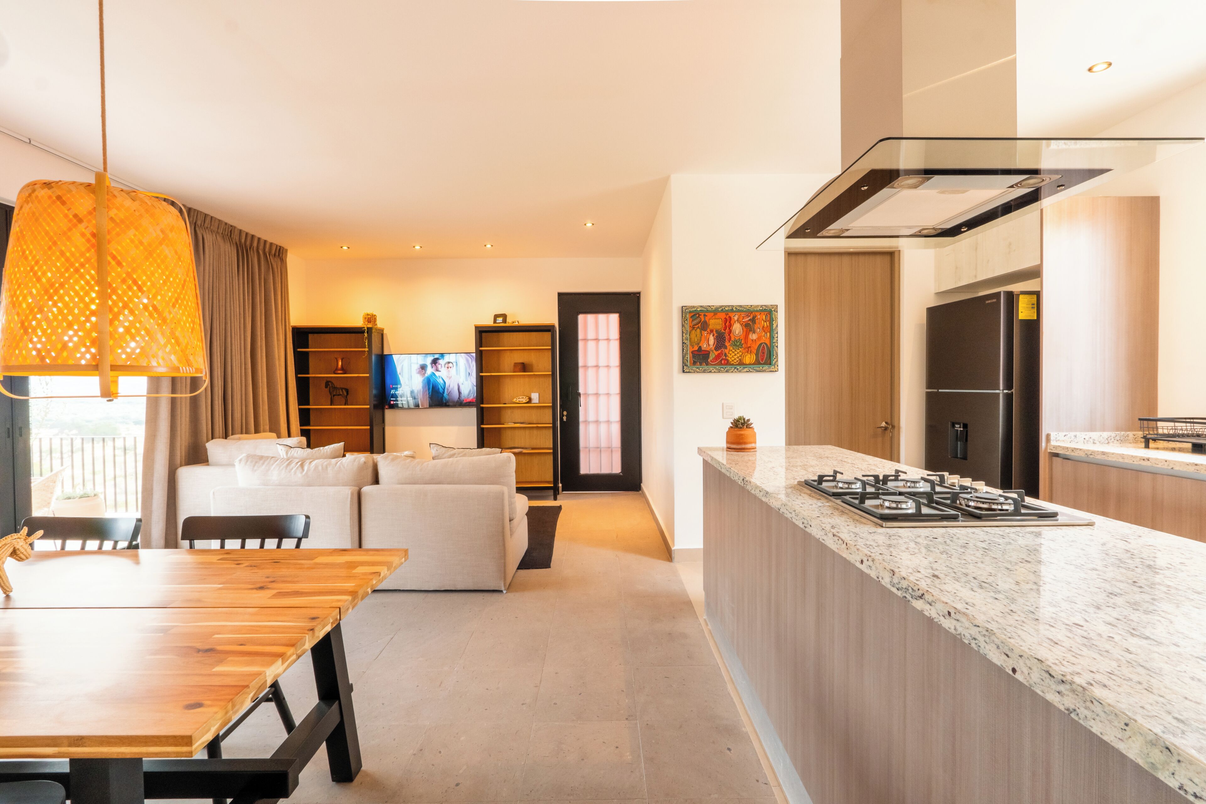 A modern kitchen with a built-in gas stove, a dining area with a wooden table, and a living room with a sofa and TV.