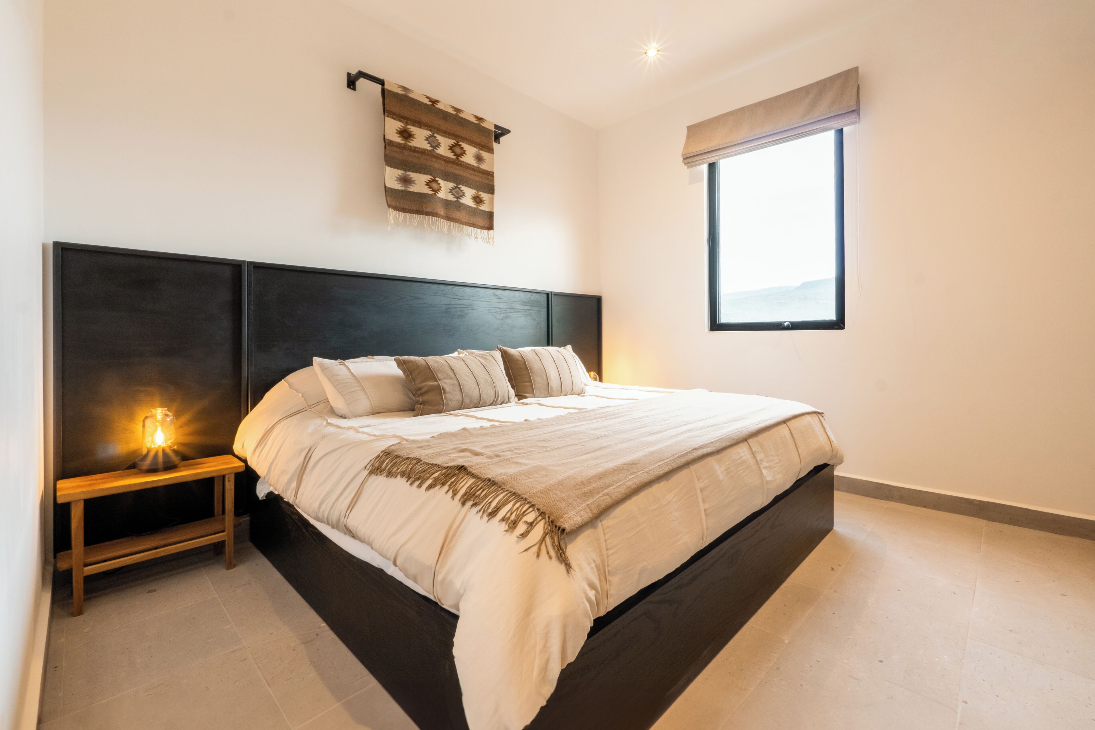 Une chambre avec un grand lit, une table de chevet avec une lampe, une fenêtre donnant sur un beau paysage et un objet décoratif fixé au mur.