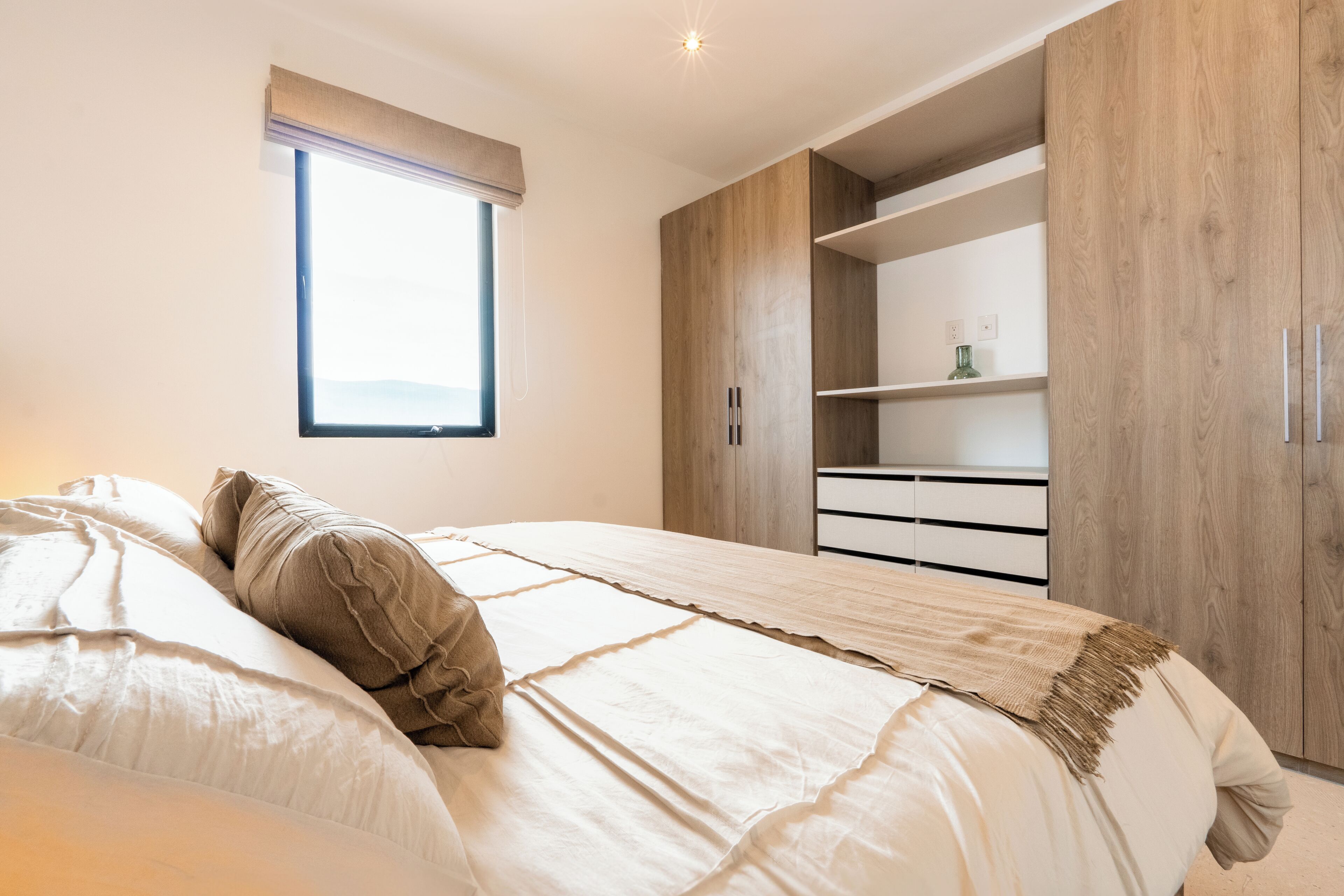 A bedroom with a large bed, a window with a view, built-in wooden wardrobe, and a bedside table.