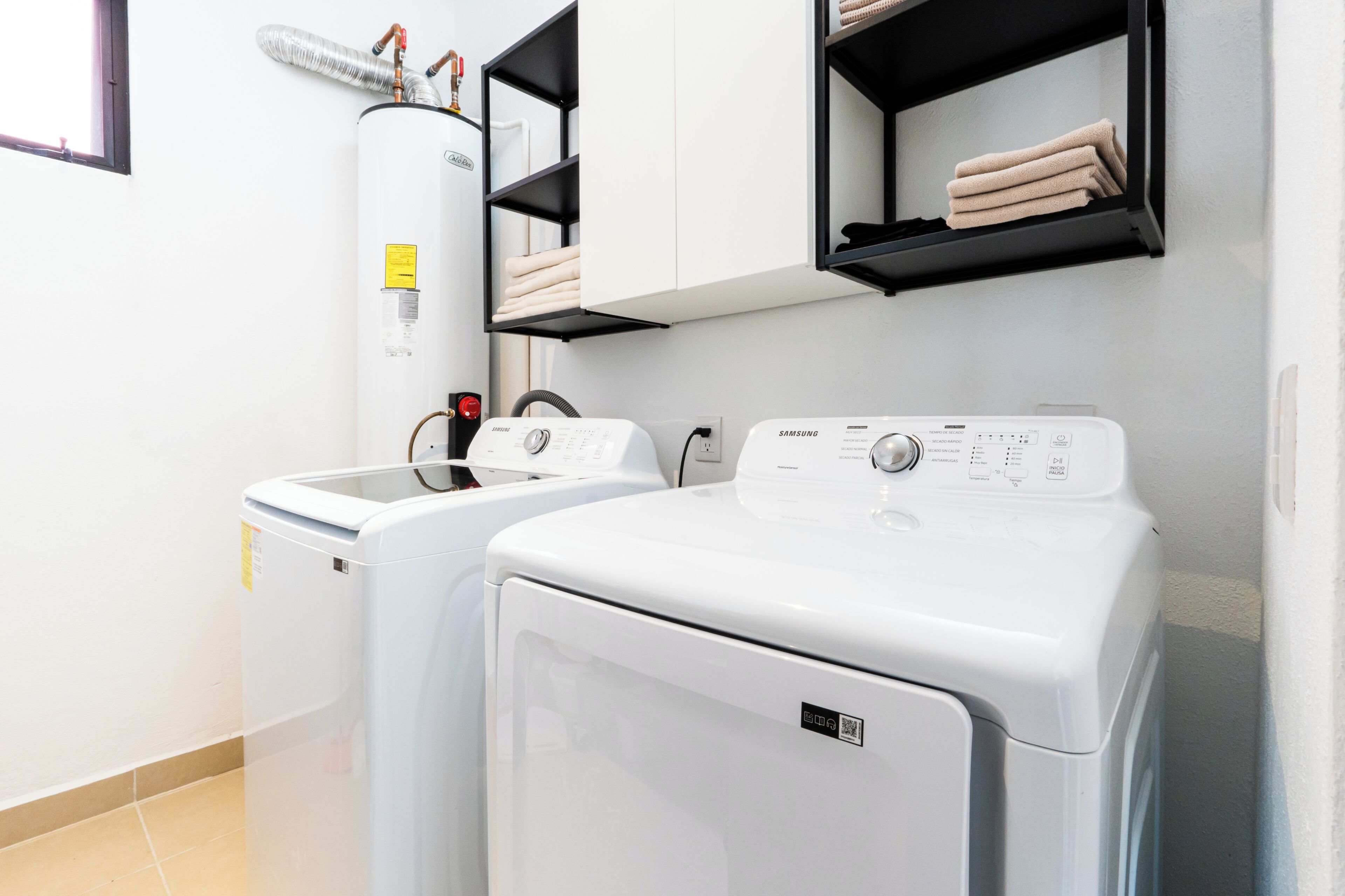 A laundry area with two white washing machines, a water heater, and shelves with folded towels.