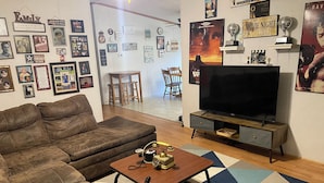 Olohuoneessa on ruskea nahkasohva, valokuvakameralla varustettu sohvapöytä, litteänäyttöinen televisio ja kuviollinen matto.