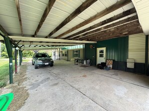 A covered parking area with a vehicle, a table, and a door. - Jetted Tub, Private Acre, Peaceful 3BR Retreat. Pet-Friendly. 15 Min to Louisvil (Lanesville)