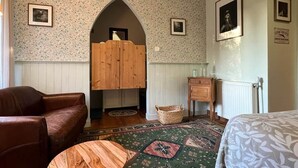 A room with a wooden arched doorway, a brown leather sofa, a patterned rug, and a bed with a floral bedspread. - defaultName (Le Mené)