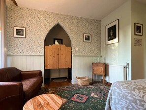 Ein Zimmer mit einer holzverzierten Bogenöffnung, einem braunen Ledersofa, einem gemusterten Teppich und einem Bett mit floralem Überwurf.
