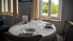 A dining table set with plates, glasses, and cutlery, positioned near a window with a view of greenery. - defaultName (Le Mené)