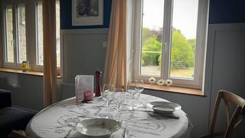 A dining table set with plates, glasses, and cutlery, positioned near a window with a view of greenery.