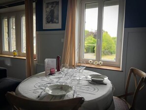 Ein Esstisch mit Tellern, Gläsern und Besteck, nahe einem Fenster mit Blick auf Grünflächen.