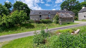 A stone building with a sloped roof, surrounded by greenery and a clear sky. - defaultName (Le Mené)