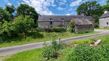 A stone building with a sloped roof, surrounded by greenery and a clear sky.