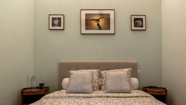 A bedroom with a bed, two nightstands, and three framed pictures on the wall. - defaultName (Le Mené)