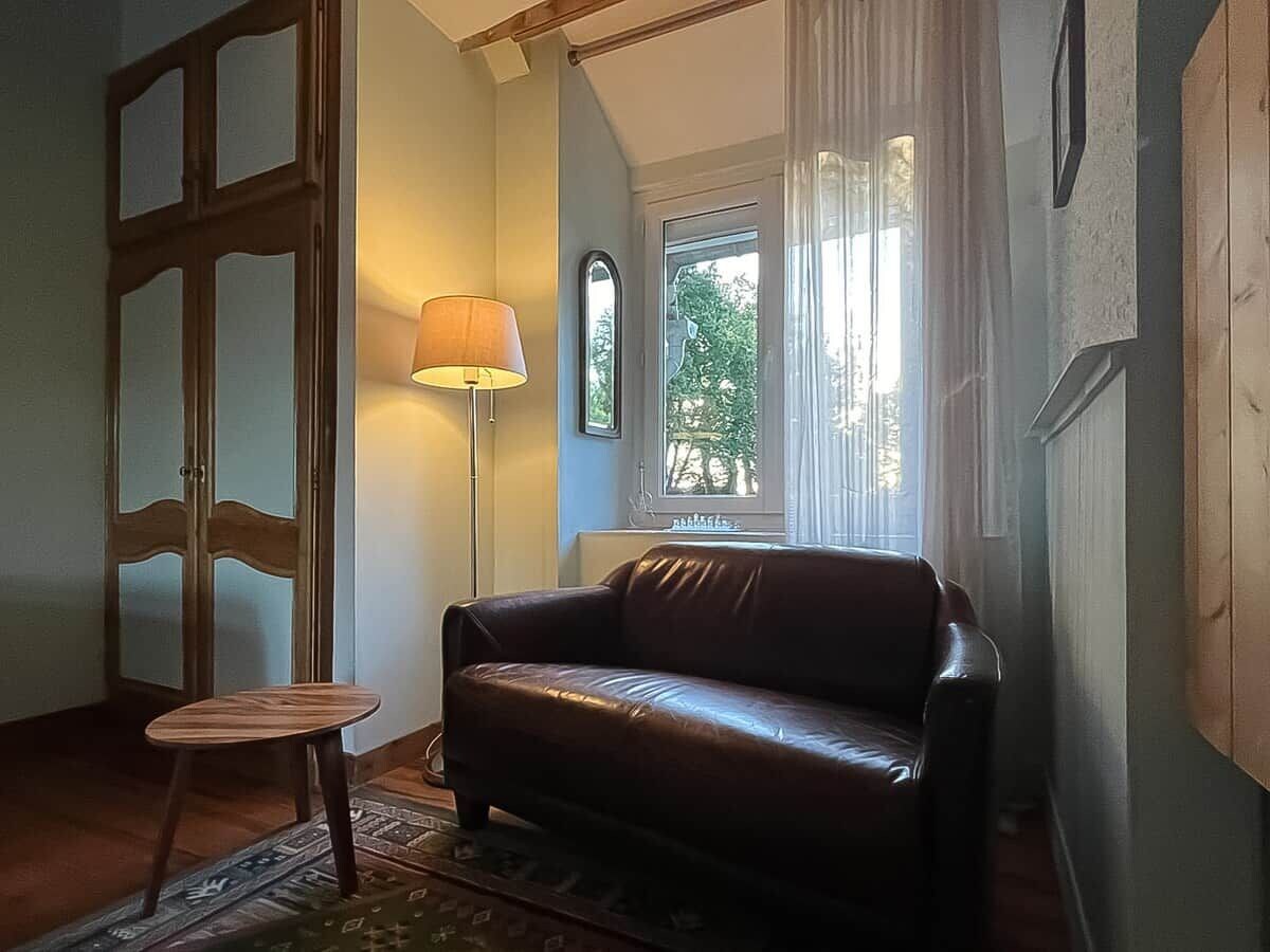 Une pièce avec un canapé en cuir, une petite table ronde, un lampadaire et une fenêtre avec des rideaux.