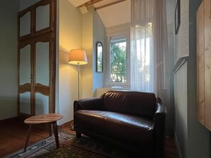 Una habitación con un sofá de cuero, una mesita redonda pequeña, una lámpara de pie y una ventana con cortinas.