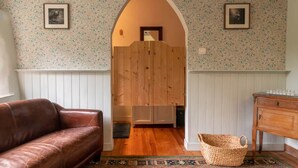 A room with a brown leather sofa, a wooden wardrobe, a woven basket, and a patterned rug. - defaultName (Le Mené)