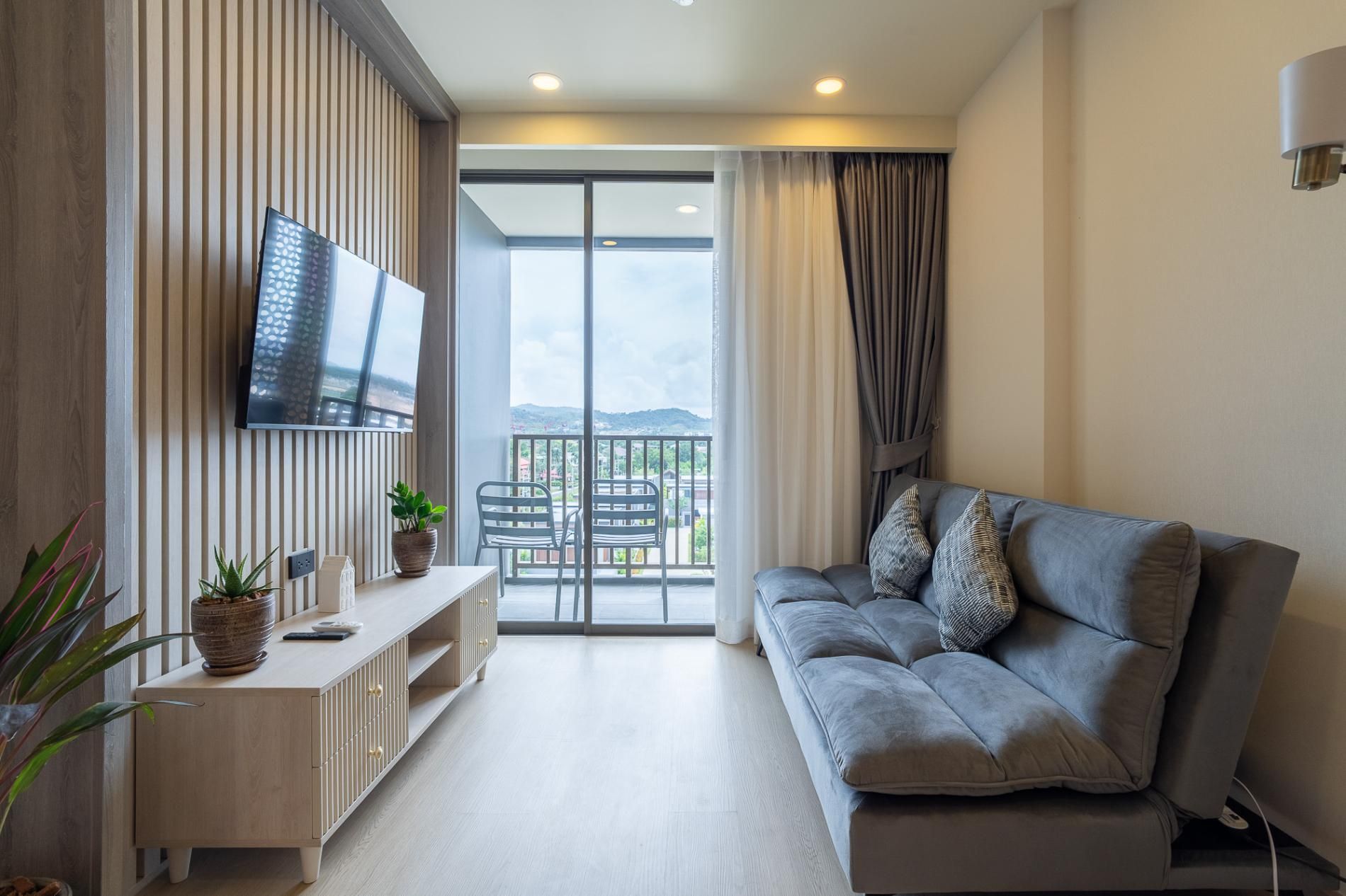 Un salon moderne avec un canapé, un téléviseur, un balcon offrant une vue et une plante posée sur une console.