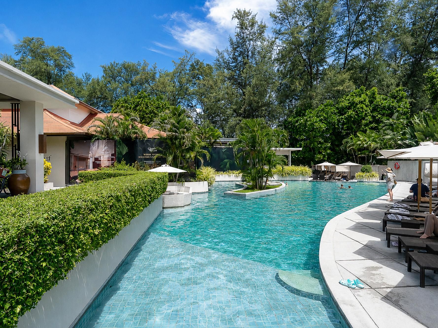 Une piscine dont le bord est revêtu de carrelage, entourée de verdure et de chaises longues.