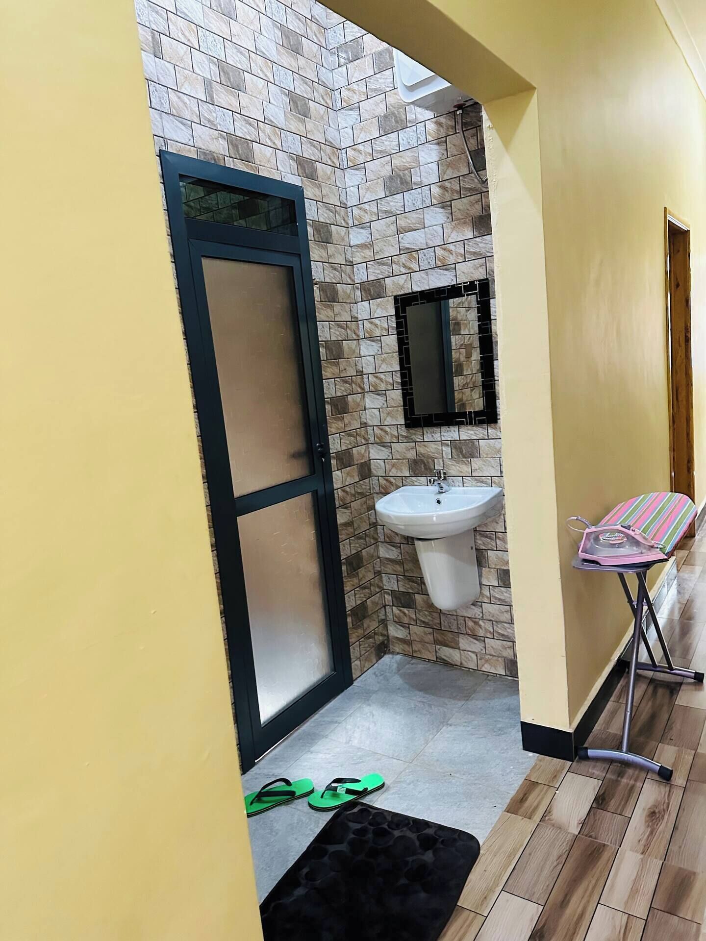 A narrow hallway leading to a bathroom with a tiled wall, a sink, and a door.