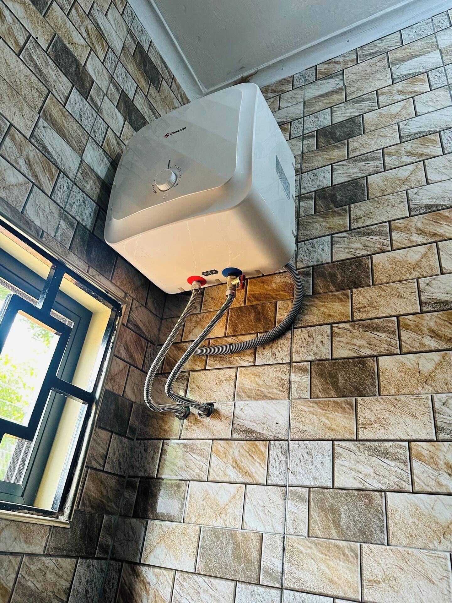 Un chauffe-eau fixé sur un mur recouvert de carreaux, avec une fenêtre sur le côté gauche.