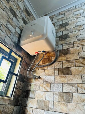 Un chauffe-eau fixé sur un mur recouvert de carreaux, avec une fenêtre sur le côté gauche.