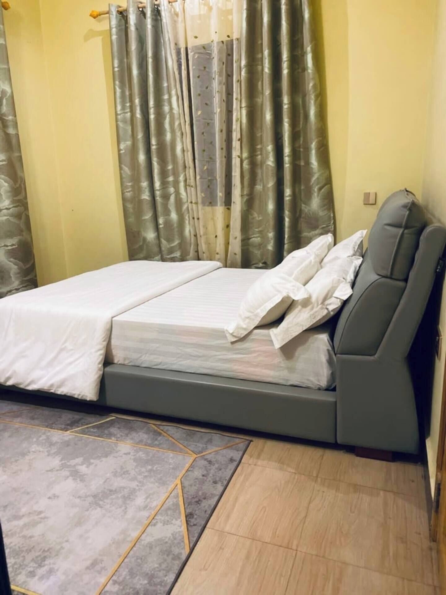 A bedroom with a bed, grey curtains, and a grey sofa.