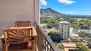 Ein Balkon mit zwei Holzstühlen und Blick auf eine Stadtlandschaft mit Gebäuden und einem Berg.