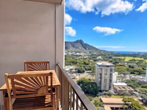 A balcony with two wooden chairs and a view of a cityscape with buildings and a mountain. - 23F-Waikiki Gem-1BR Condo with Diamond Head & Ocean Views (Honolulu)