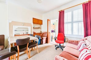 Un espacio habitable compacto con una mesa de comedor, sillas, un sofá y una cocina visible a través de una puerta abierta.