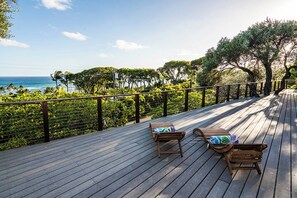 A wooden deck with two lounge chairs and a railing overlooking a beach and ocean. - Diamond Head Tranquility: 4BR Ocean View Home (Honolulu)