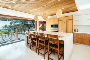 A modern kitchen with wooden cabinets, a large island with bar stools, and pendant lighting. - Diamond Head Tranquility: 4BR Ocean View Home (Honolulu)