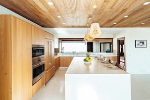 Eine moderne Küche mit Holzausbau, Edelstahlgeräten und einer zentralen Kochinsel mit Obst und Gläsern.