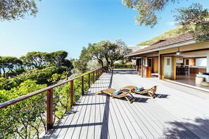 Eine Holzterrasse mit Liegestühlen, einem Geländer und einem Gebäude mit Küchenbereich.