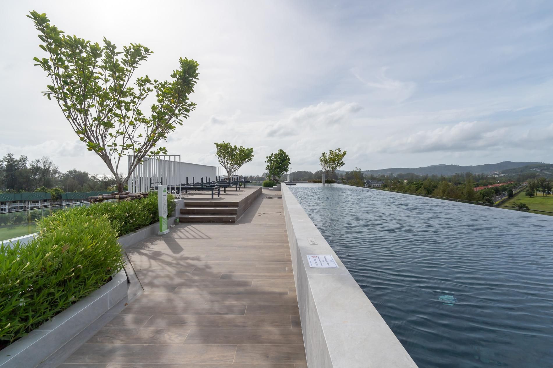 Una piscina con un paseo empedrado, rodeada de vegetación y vistas a colinas distantes.