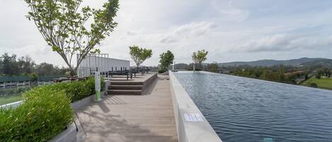 Una piscina con un paseo empedrado, rodeada de vegetación y vistas a colinas distantes.