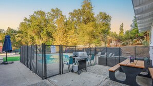 A backyard with a pool, grill, seating area, and a fenced enclosure.