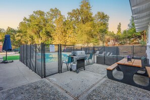 A backyard with a pool, grill, seating area, and a fenced enclosure.
