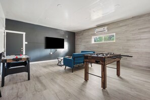 Un salon moderne avec un baby-foot, un téléviseur à écran plat fixé au mur et un canapé bleu.