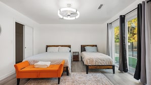 A bedroom with two beds, a bench, a ceiling light, and a view of the outdoors.