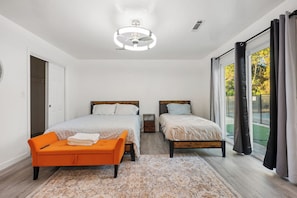 A bedroom with two beds, a bench, a ceiling light, and a view of the outdoors.