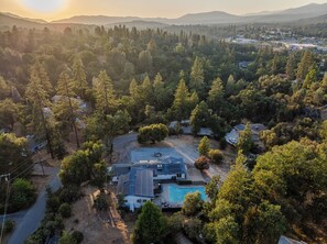 A residential area with a house featuring a swimming pool, surrounded by dense forest and hills in the background. - Yosemite Gateway Oasis - A Spacious 7 Bedroom house with pool (Oakhurst)