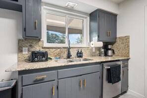 A modern kitchen with granite countertops, a built-in stove, a coffee maker, and a window above the sink. - Yosemite Gateway Oasis - A Spacious 7 Bedroom house with pool (Oakhurst)