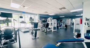 Een sportschool met diverse fitnessapparaten, waaronder loopbanden, krachttoestellen en een bank.