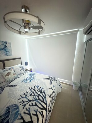Een slaapkamer met een bed, een nachtkastje, een wandlamp en een plafondarmatuur.