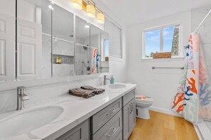 Ein modernes Badezimmer mit einem großen Spiegel, zwei Waschbecken, einer Dusche und einem Fenster.