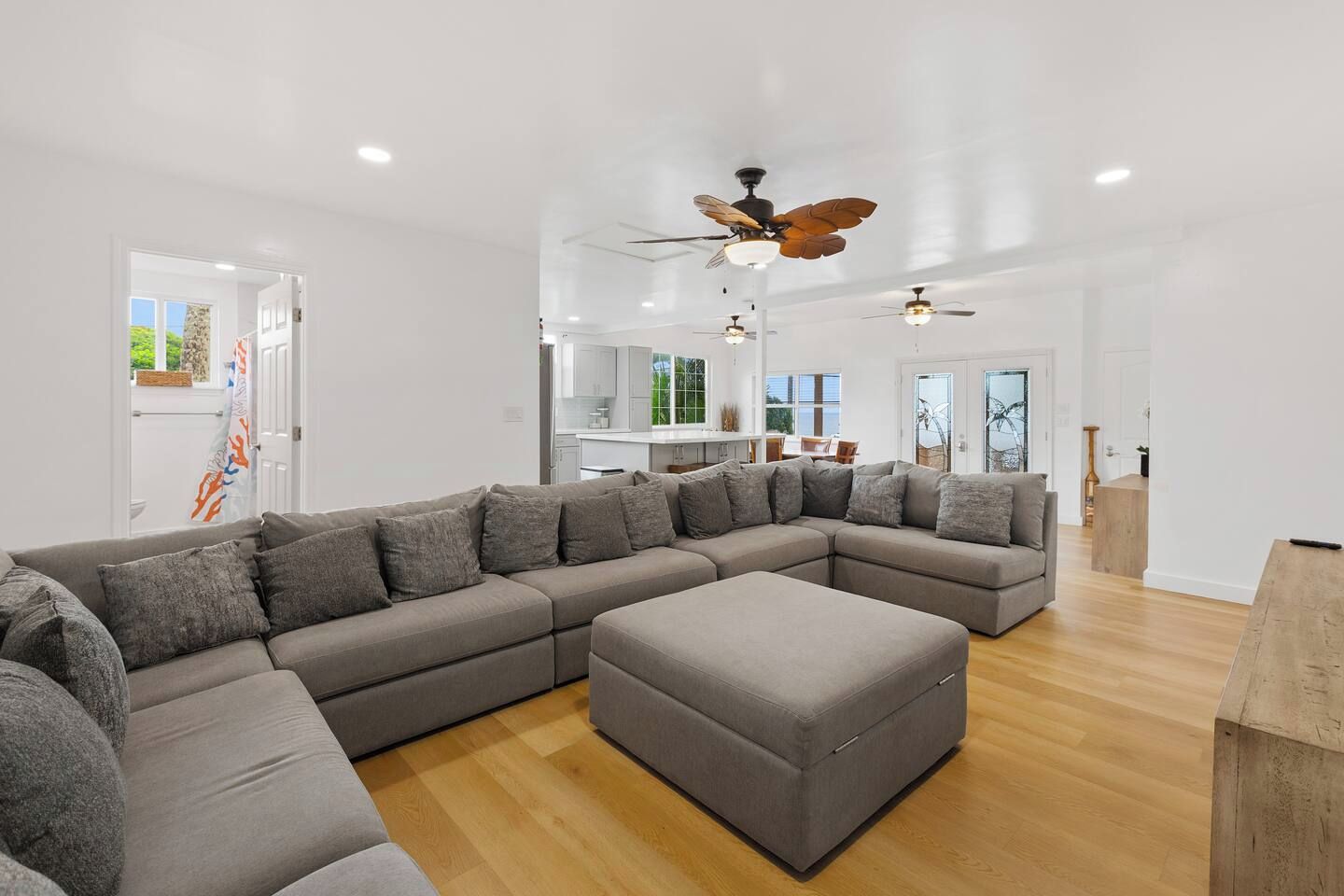 A modern living room with a large L-shaped sectional sofa, a wooden coffee table, and a ceiling fan.