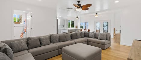 A modern living room with a large L-shaped sectional sofa, a wooden coffee table, and a ceiling fan.