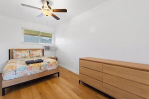 Ein Schlafzimmer mit einem Bett, einem Holzschrank, einem Deckenventilator und einem Fenster mit Jalousien.